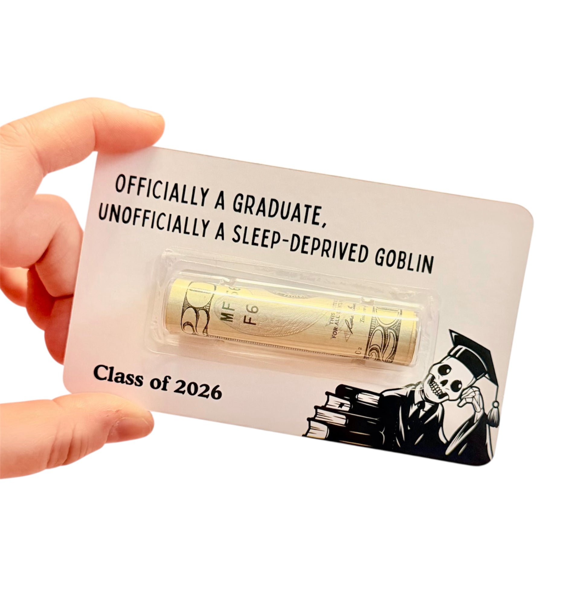 Hand holding a small card with a skeleton graduation-themed design, featuring text and graphics.
