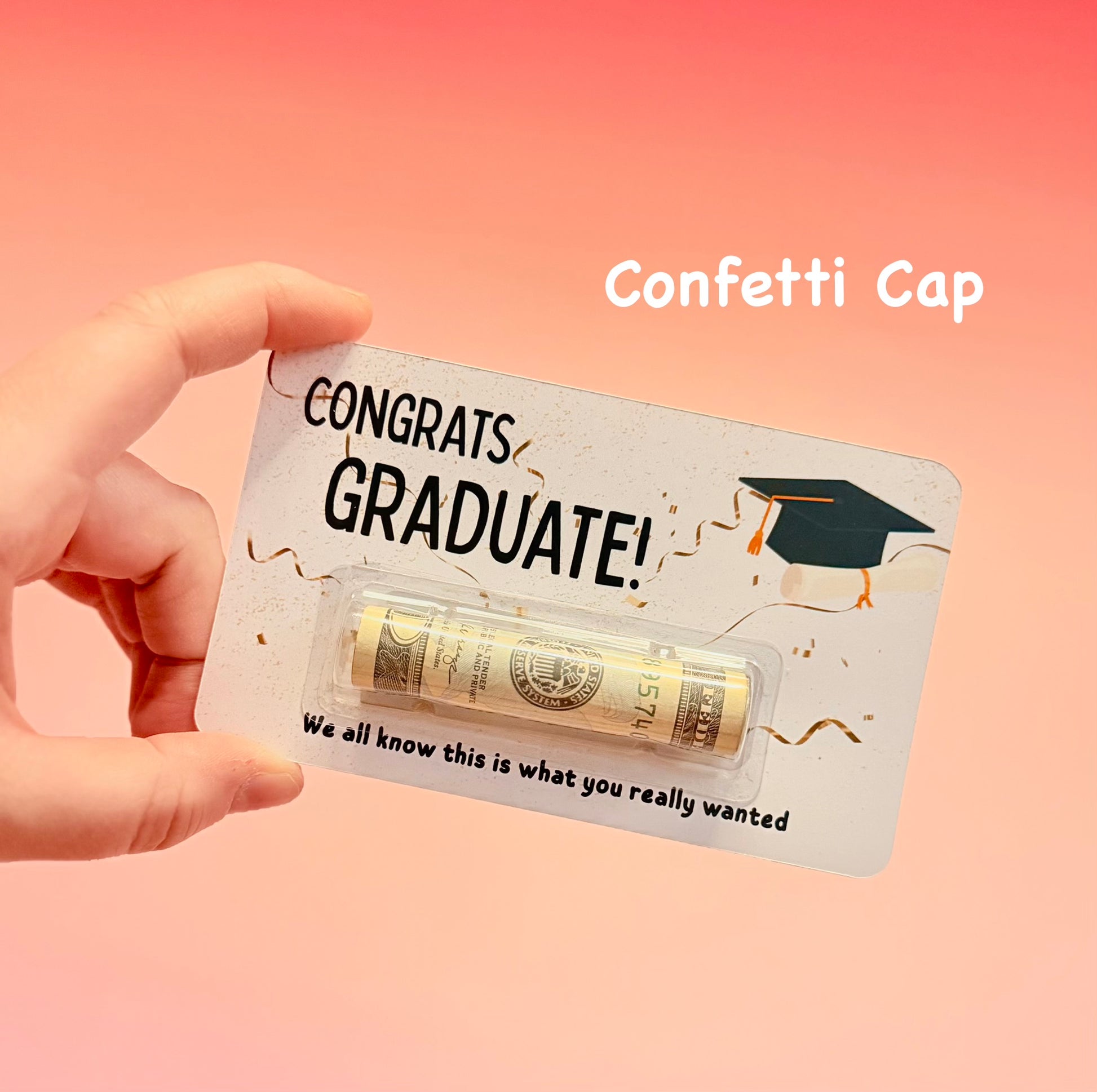 Hand holding a 'Congrats Graduate!' card with confetti cap on a pink background