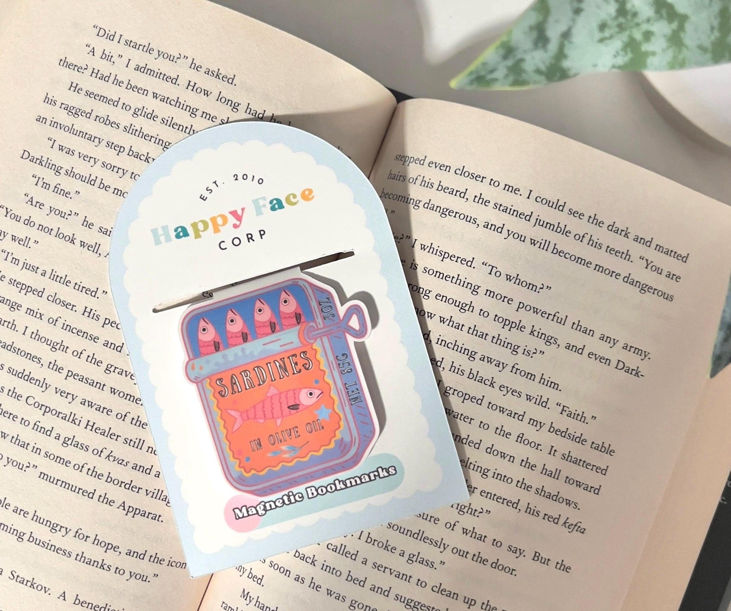 A magnetic bookmark of a pink and orange cartoon style sardine that is shown how it is packaged.