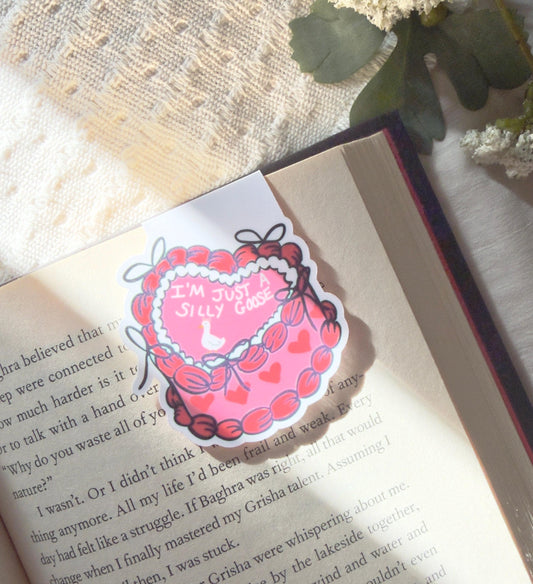 A magnetic bookmark of a red and pink frosted heart shaped cake that says just a silly goose and has an image of a very tiny white goose