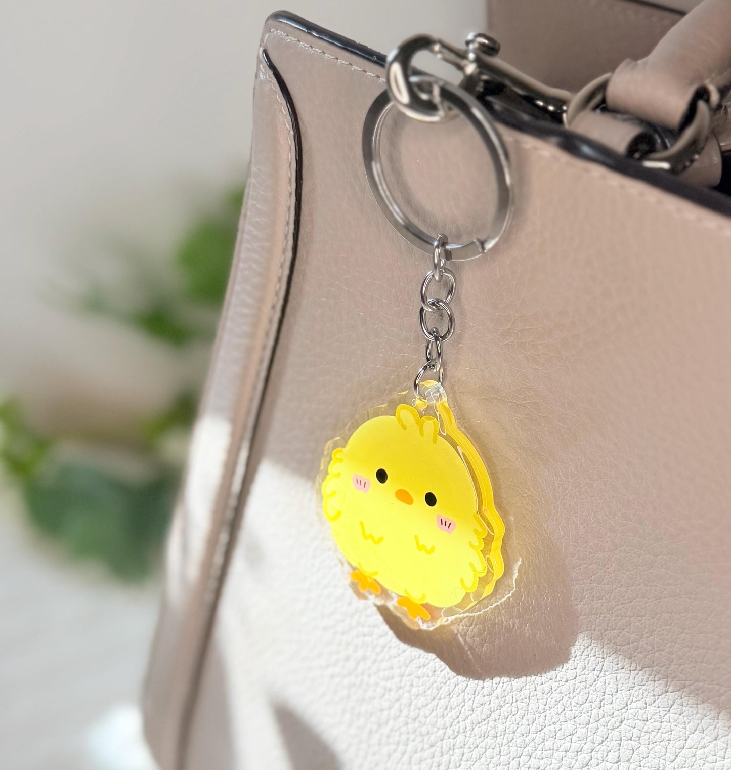 The yellow chick acrylic keychain displayed on a purse 