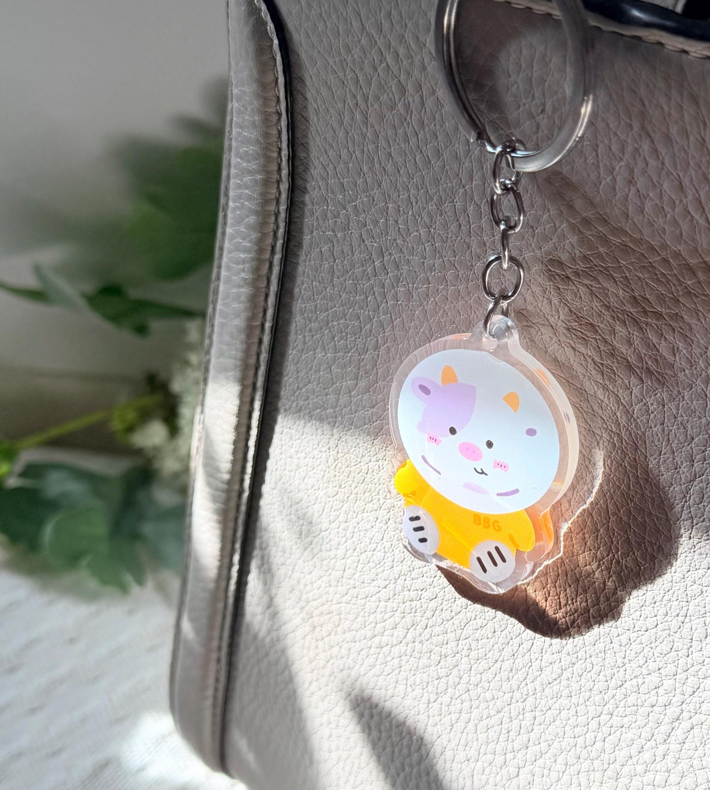 The purple space cow keychain displayed on a purse