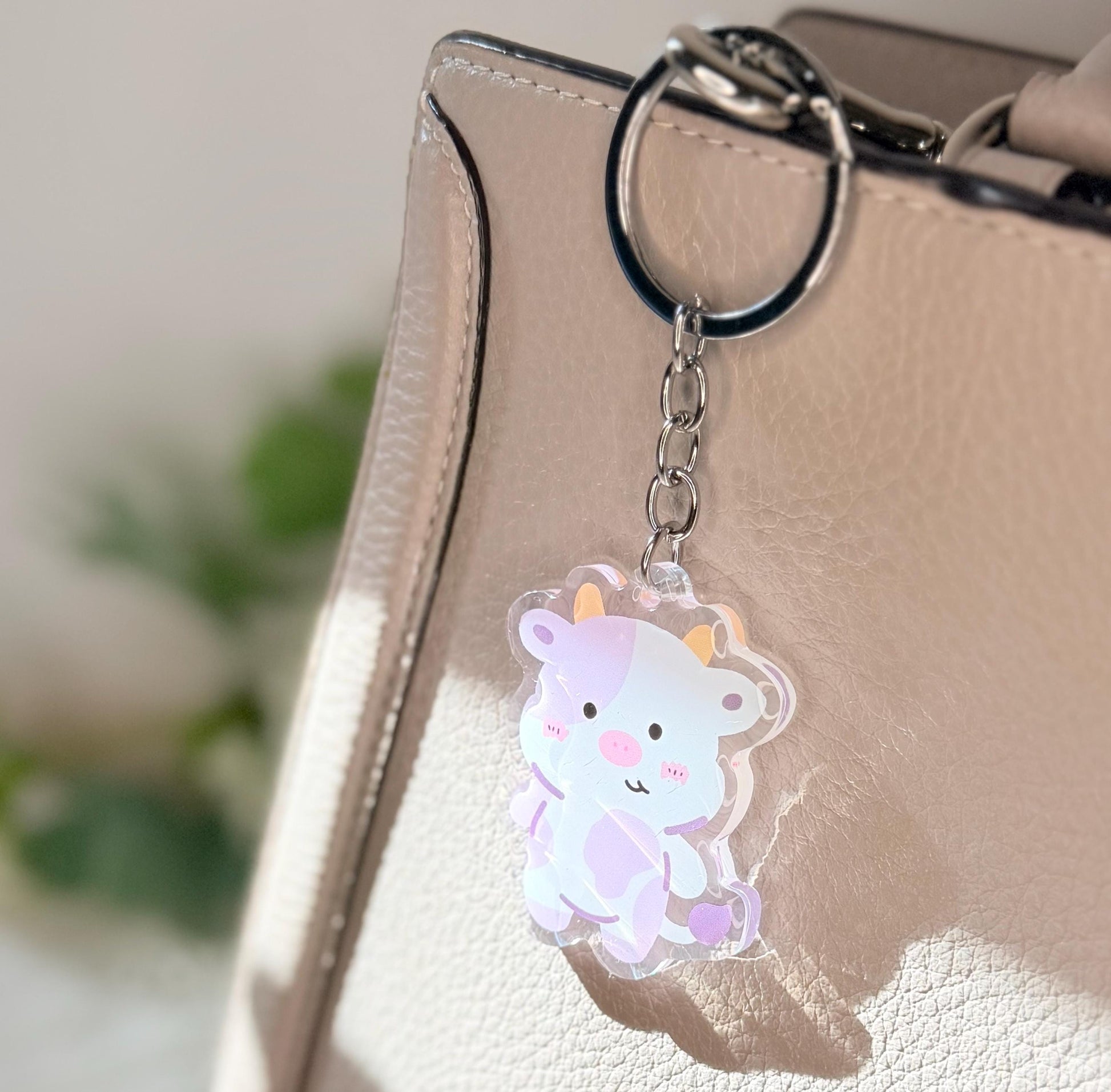 The purple cow keychain displayed on a purse
