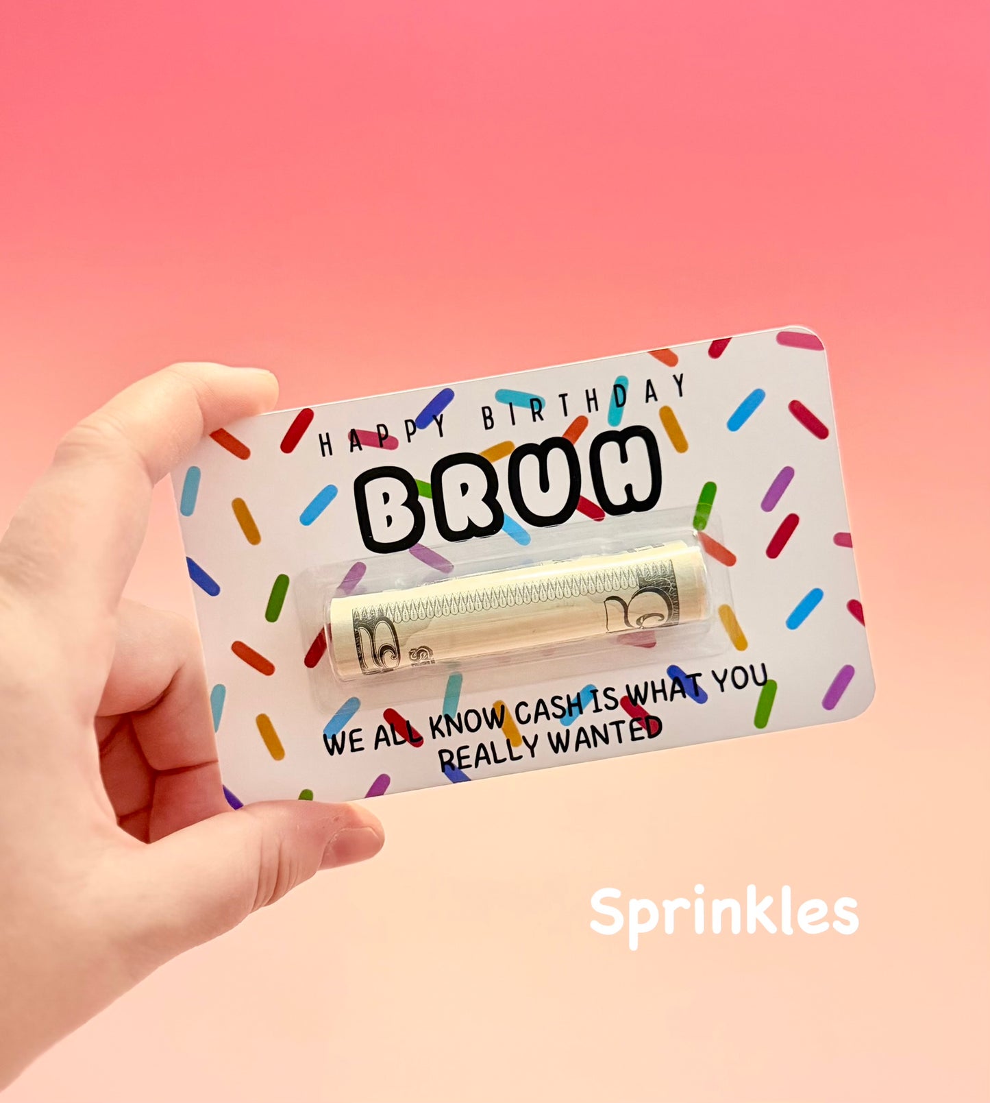 Hand holding a novelty gift card with colorful sprinkles and text on a pink background