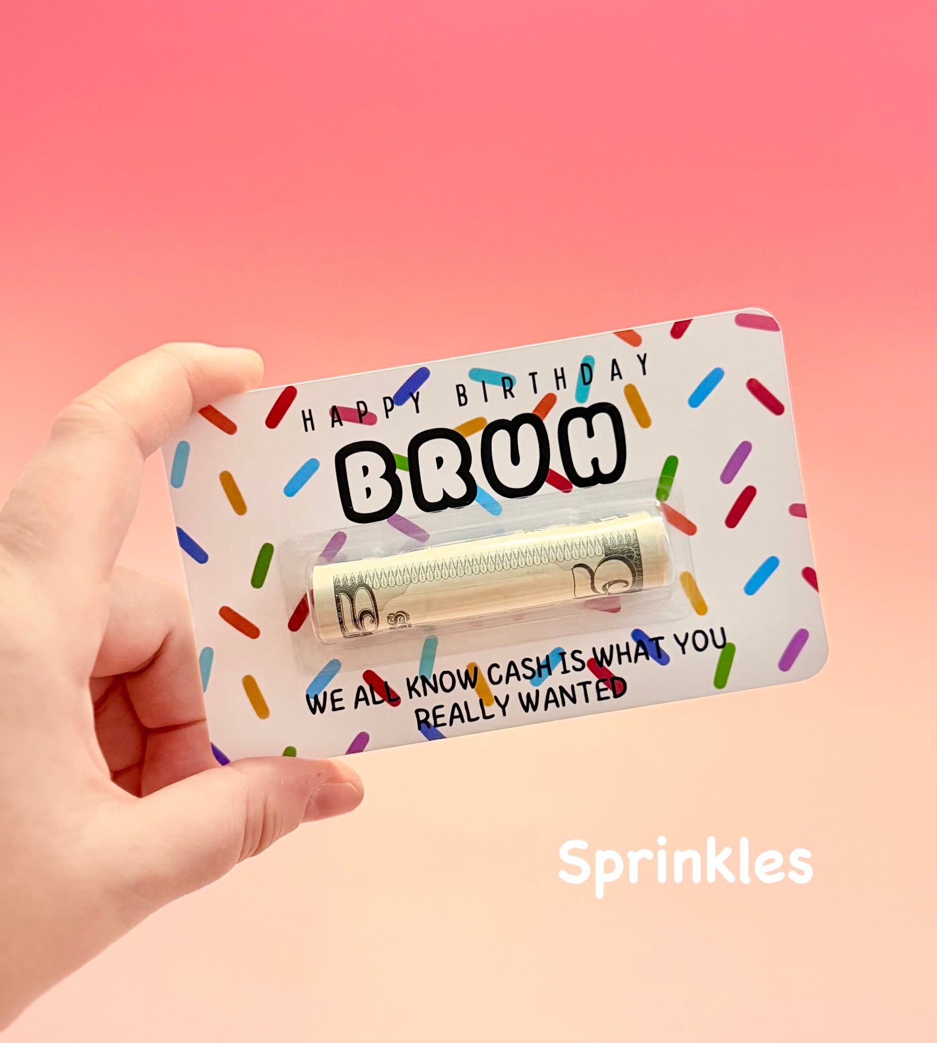 Hand holding a novelty gift card with colorful sprinkles and text on a pink background