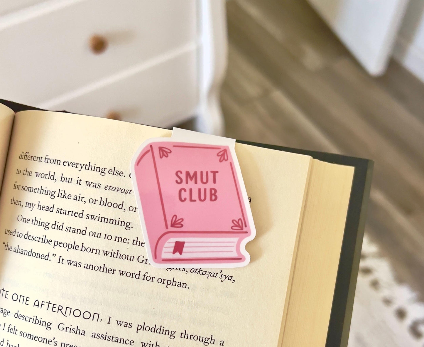 A magnetic bookmark of a plain cartoon style pink book that says smut club