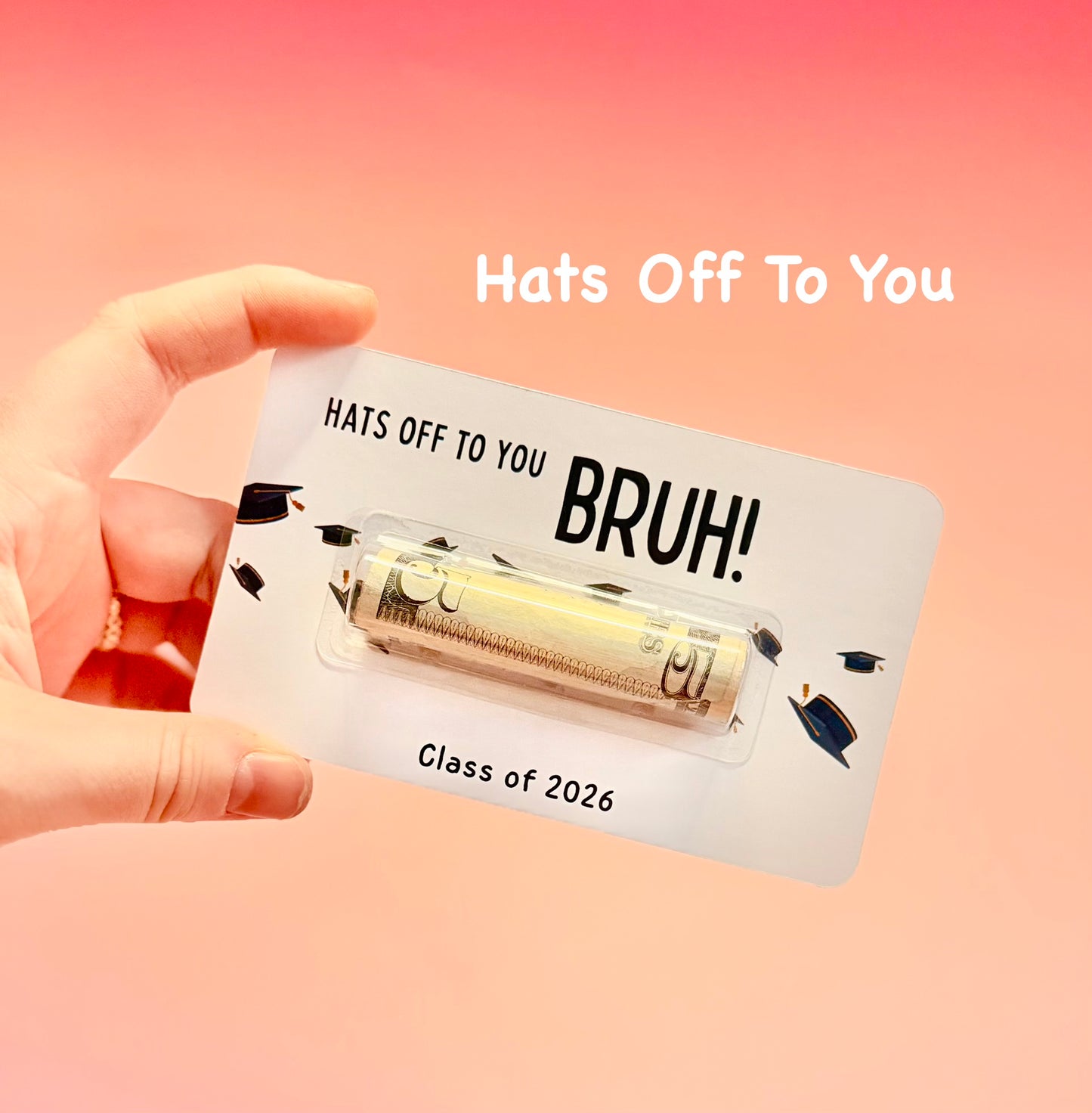 Hand holding a card with 'Hats Off To You BRUH! Class of 2026' text on a pink background