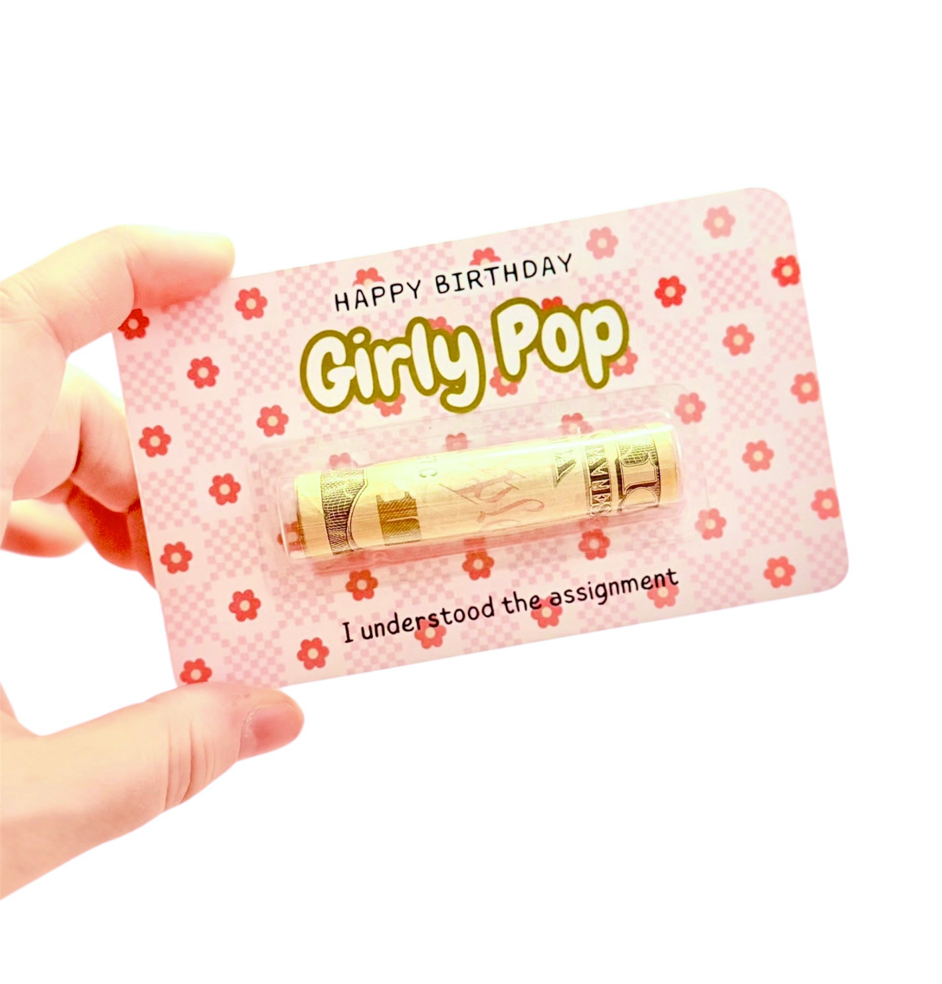 Hand holding a pink 'Happy Birthday Girly Pop' card with a small gold object on a white background