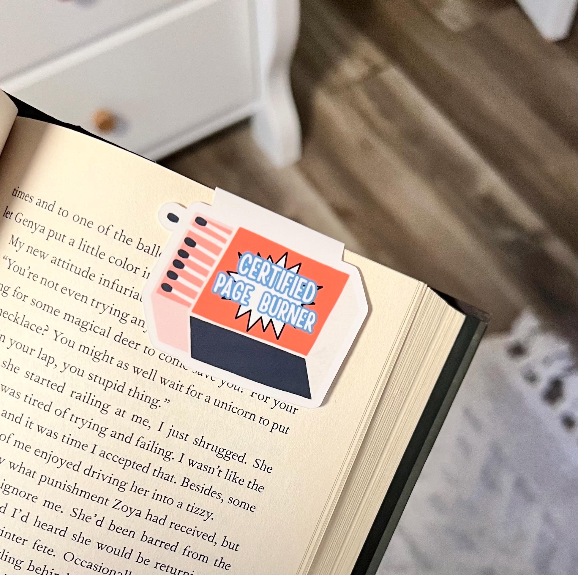 A magnetic bookmark of an orange and blue box of matches in a cartoon style that says certified page burner