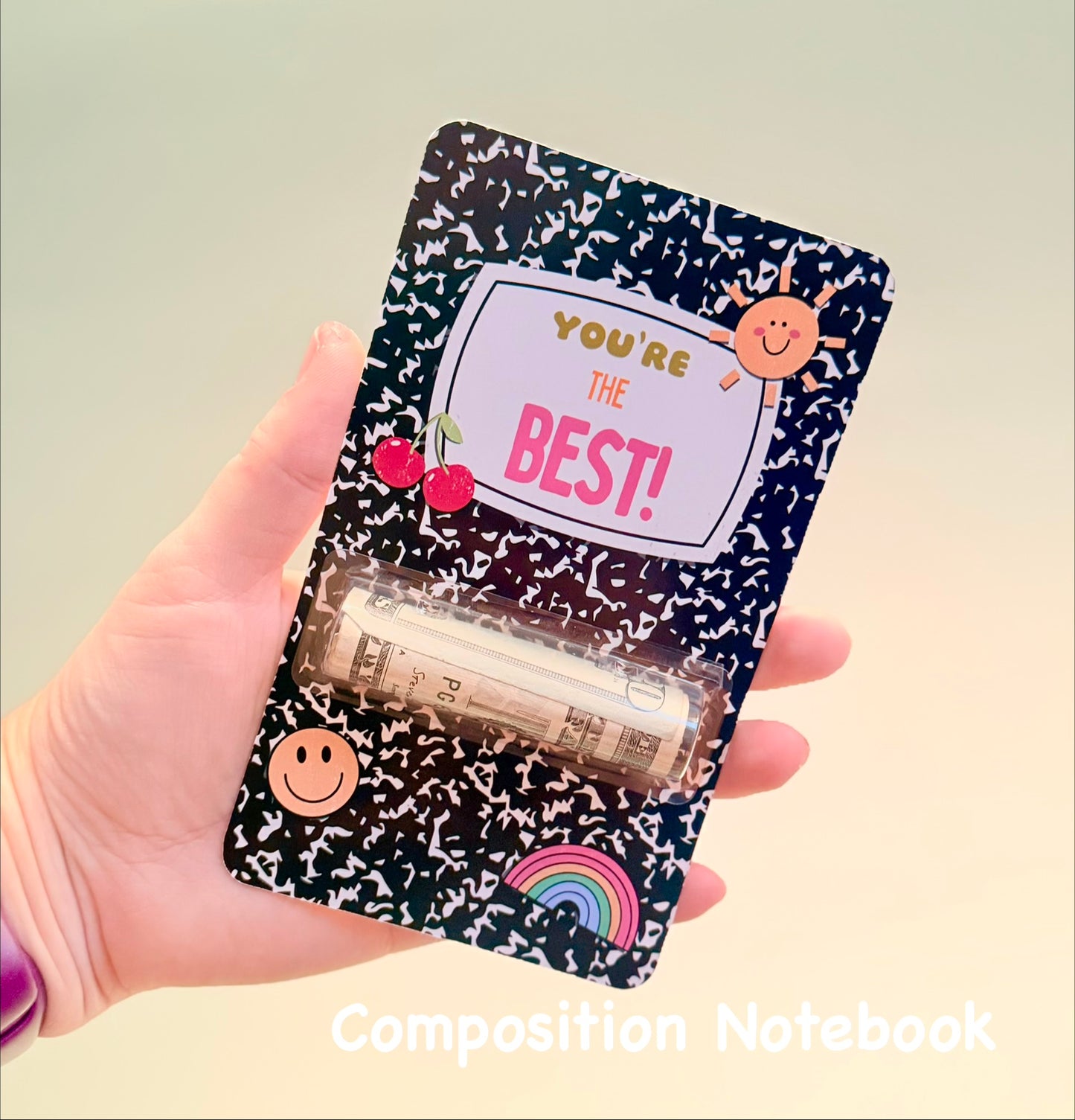 Hand holding a composition notebook style card with decorative cover and text 'You're the Best!'