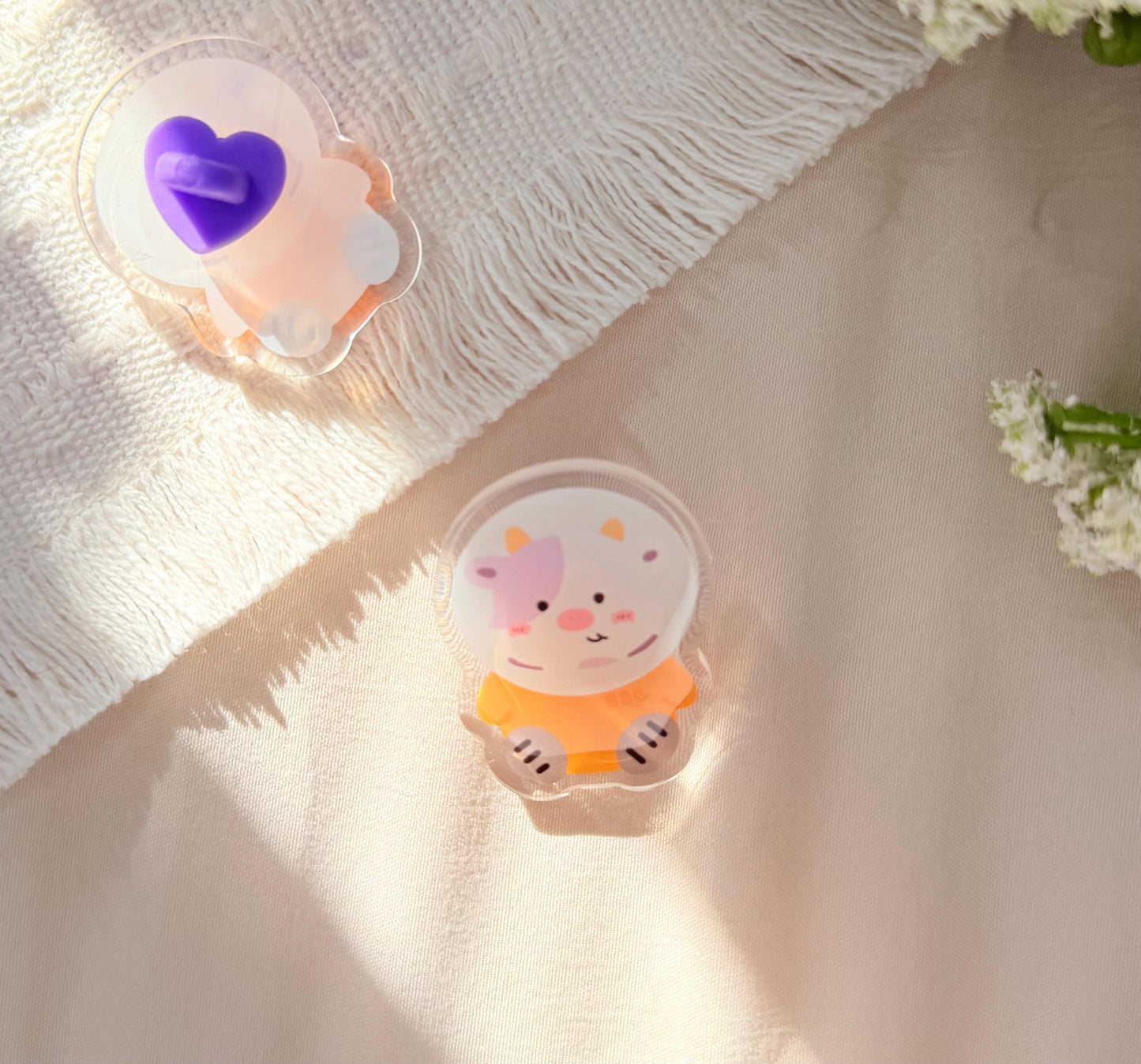 An acrylic pen of a Kawaii style purple spotted cow in an orange astronaut suit