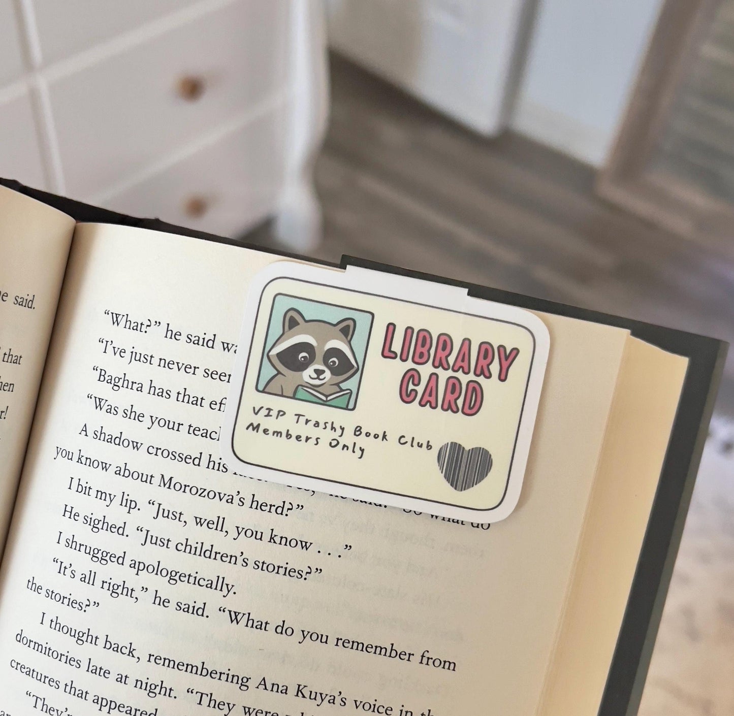 A magnetic bookmark of a raccoon on a library card style bookmark that says trashy book club