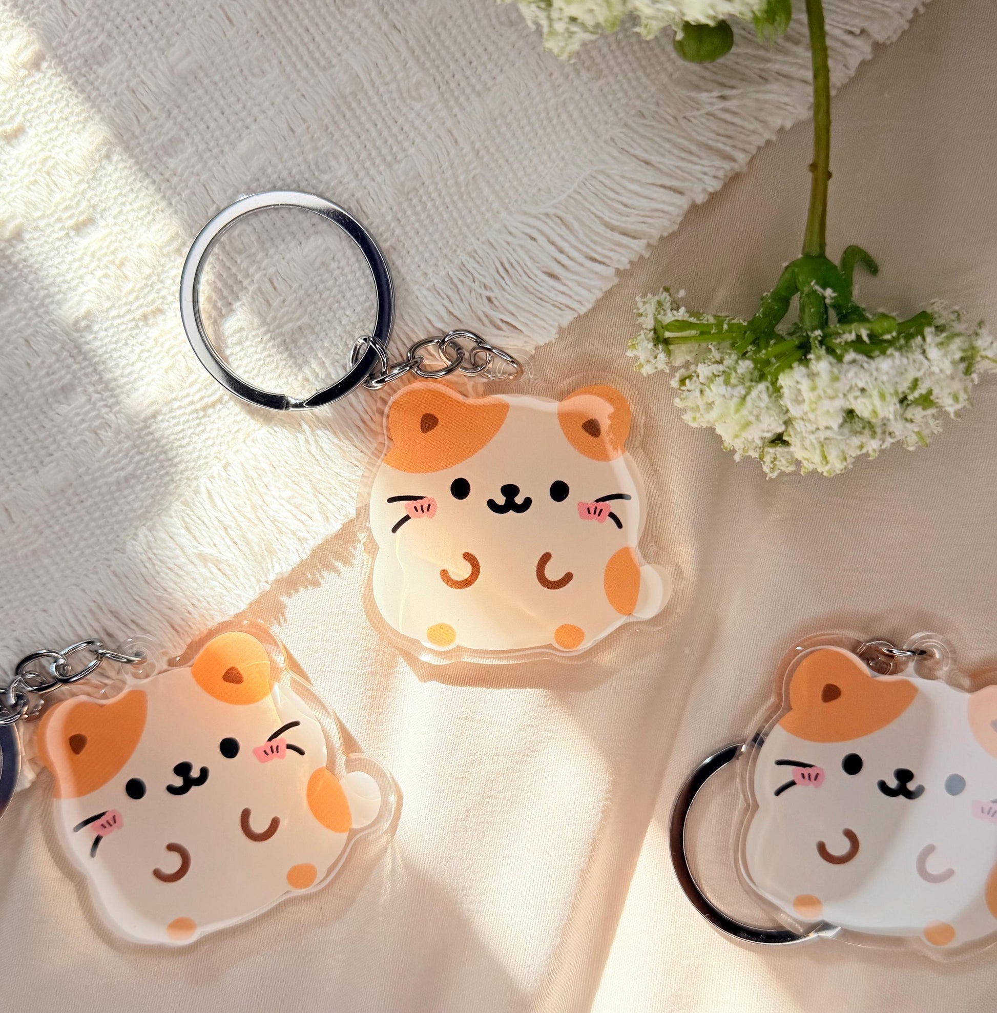 An acrylic keychain of a Kawaii style tan and white hamster