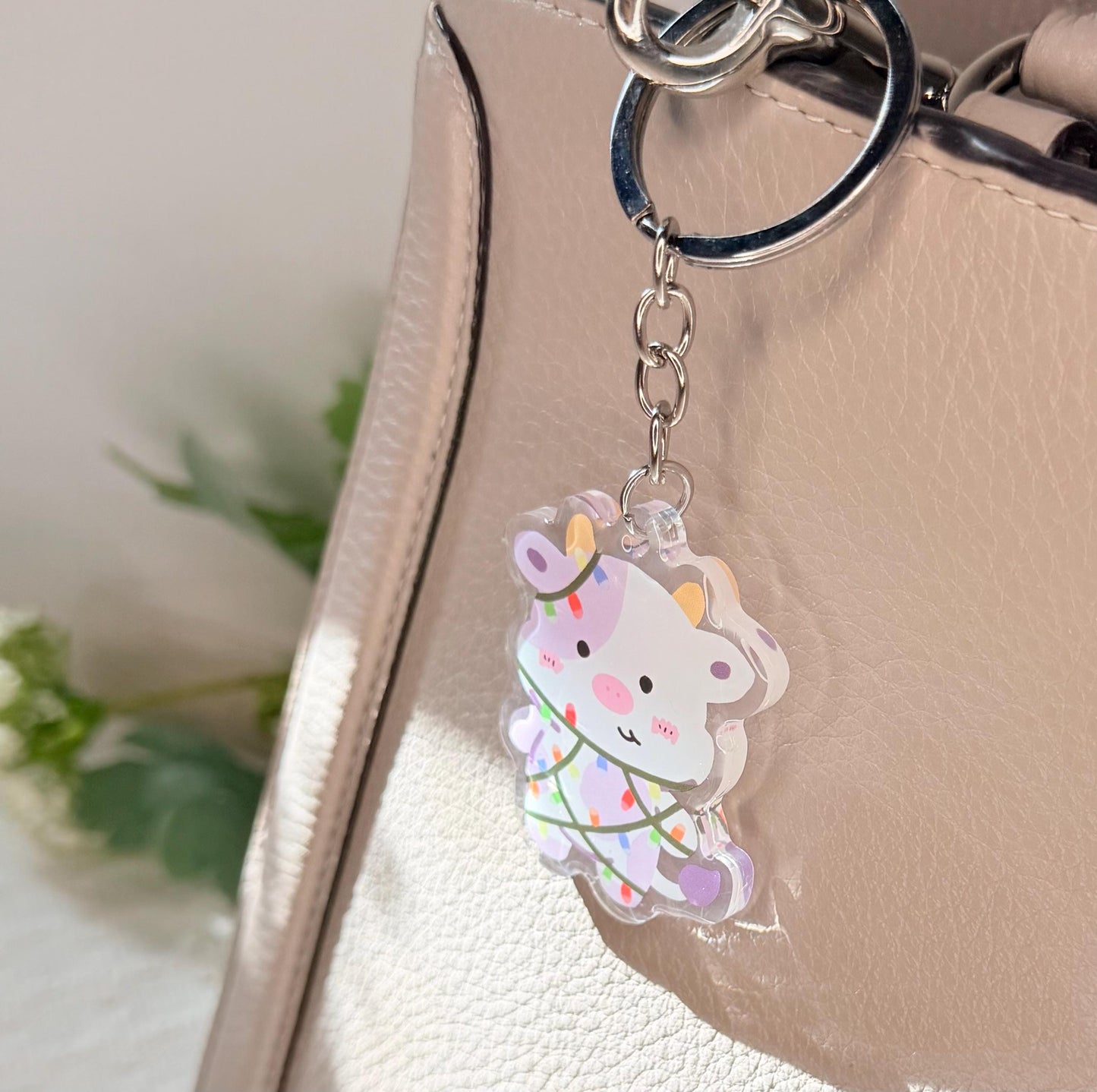 The purple cow Christmas light keychain displayed on a purse