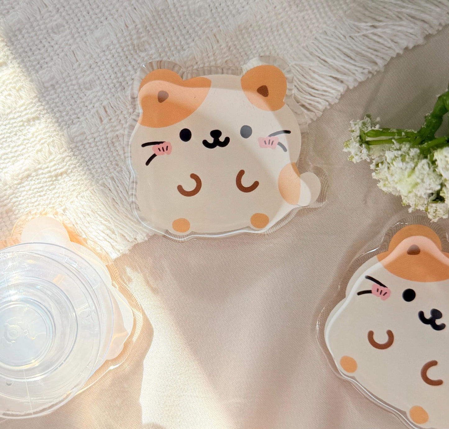 An acrylic phone grip of a Kawaii style hamster that is tan and white
