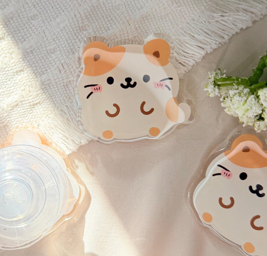 An acrylic phone grip of a Kawaii style hamster that is tan and white